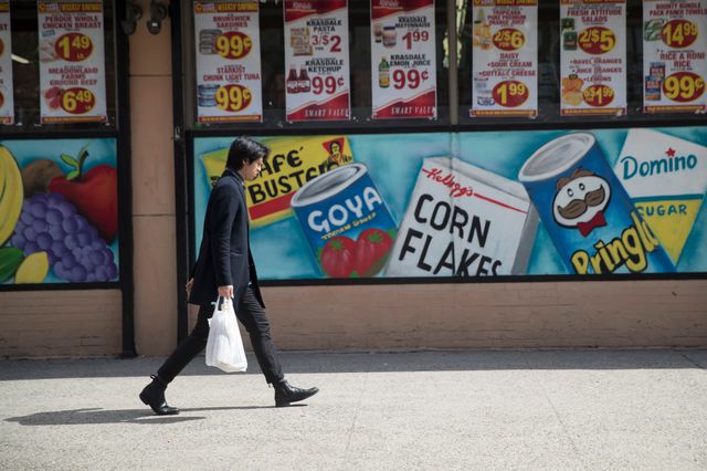 A man leaves a supermarket in the East Village neighborhood of Manhattan carrying his groceries in a plastic bag.